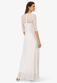 Witte lange jurk met doorschijnende kanten driekwartmouwen, een getailleerde bodice en een vloeiende rok. De achterkant heeft florale kanten details.