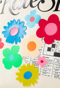 Des appliqués floraux en plastique de diverses couleurs (bleu, rose, rouge, jaune, vert) sur un fond crème texturé avec des détails imprimés de mots croisés.