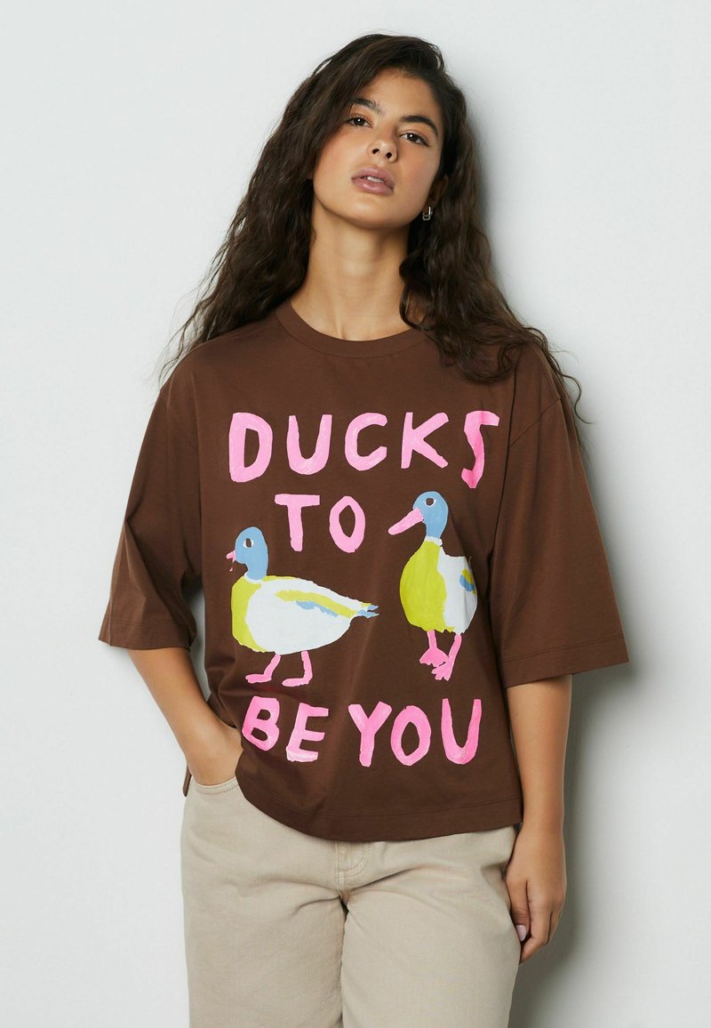 Tricou maro supradimensionat cu două rațe colorate și textul "DUCKS TO BE YOU" în roz. Mâneci scurte și decolteu rotund.
