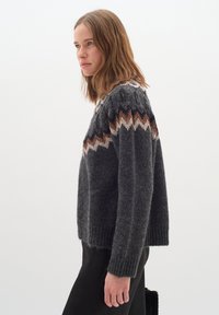 Pulover tricotat de culoare gri închis, cu decolteu rotund, având un model în zigzag multicolor în nuanțe de maro și crem la umeri.