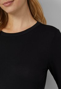 Czarna bluzka z długim rękawem, z okrągłym dekoltem, gładką fakturą i dopasowanym krojem, widoczna od klatki piersiowej w górę.