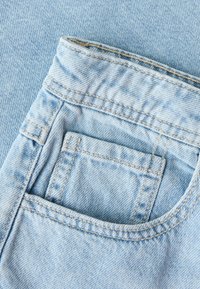 Tissu en jean bleu clair montrant la poche avant et la petite poche à monnaie avec des détails de couture visibles.