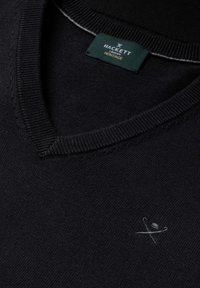 Sort V-hals sweater med et lille krydset paraply- og stoklogo nær brystet og en mørkegrøn Hackett London Heritage-mærkat inde i kraven.