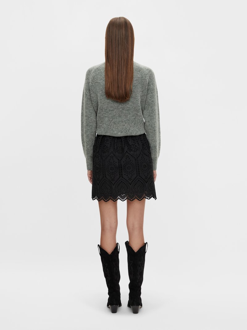Grauer Strickpullover, schwarzer Spitzenrock mit gewelltem Saum und knielangen schwarzen Wildlederstiefeln mit spitzem Schaft und dekorativen Nähten.