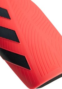 Suela roja de botas de fútbol con superficie texturizada, que presenta una prominente franja negra y pequeñas perforaciones para mayor agarre. Diseño curvado y contorneado.