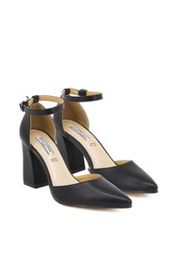 Scarpe con tacco alto in pelle nera, con punta affusolata, ritagli angolari e cinturini alla caviglia. Tacco a blocco spesso e texture liscia.