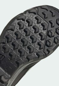 Suela de zapato negra con un patrón de agarre texturizado y multidireccional que presenta formas hexagonales y triangulares para una mejor tracción.