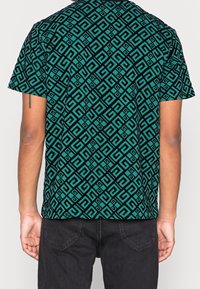 T-shirt a maniche corte in turchese e nero con un motivo geometrico, realizzata in tessuto morbido con una vestibilità rilassata e scollatura a girocollo.