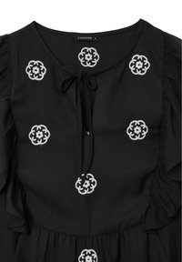 Blusa nera con motivi floreali ricamati in bianco, spalle arricciate e chiusura a fiocco sul collo.