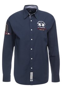Camisa de manga larga azul marino en mezcla de algodón, con cuello abotonado, logo bordado y una etiqueta lateral con instrucciones de cuidado.