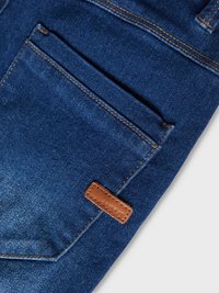 Dark blue denim fabric with a smooth texture. Features a brown leather tag and contrasting yellow stitching on the pocket edges.