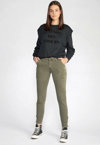 Svart genser med teksten "LE TEMPS DES AMOURS", olivengrønne cargobukser og svarte høye joggesko med hvite såler.