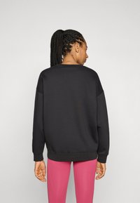 Sudadera negra de corte relajado, con puños acanalados y cuello redondeado, combinada con leggins rosas. Diseño simple, textura suave.