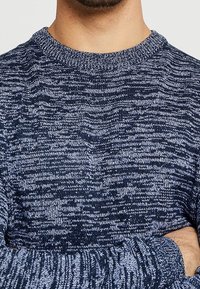 Maglione lavorato a maglia blu navy con pattern testurizzato in filato misto. Collo a giro, maniche lunghe, polsini a coste. Il materiale sembra accogliente e informale.