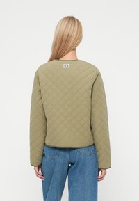 Kurtka w oliwkowym kolorze, pikowana, z długimi rękawami, okrągłym dekoltem i skróconym dołem; posiada naszywkę z logo blisko tylnego dekoltu.