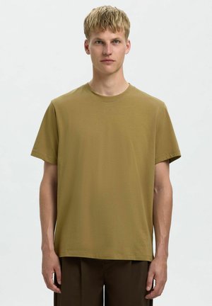 T-shirt à col rond à manches courtes vert olive en tissu doux, présentant une coupe décontractée et des détails de couture minimalistes, porté avec un pantalon marron.