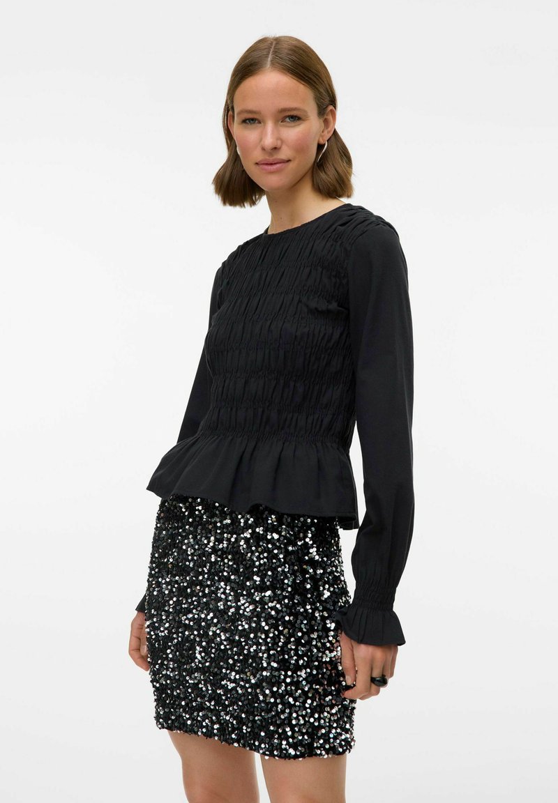 Zwarte lange mouwen top met gerimpelde textuur en peplum ontwerp, gecombineerd met een korte, met pailletten bedekte rok met reflecterende zilveren accenten.