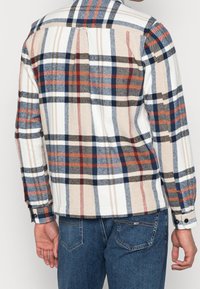 Kostkovaná flanelová košile s bílým, béžovým a modrým vzorem, s dlouhými rukávy, zapínáním na knoflíky u manžet a klasickým límcem.