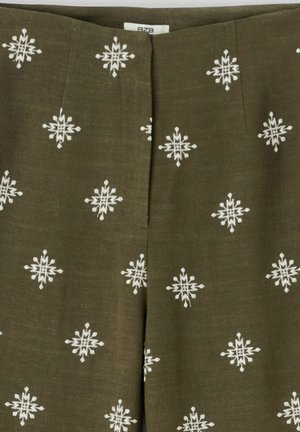 Tissu vert olive avec un motif brodé géométrique blanc en forme d'étoile, présentant une couture centrale et une petite étiquette visible en haut.
