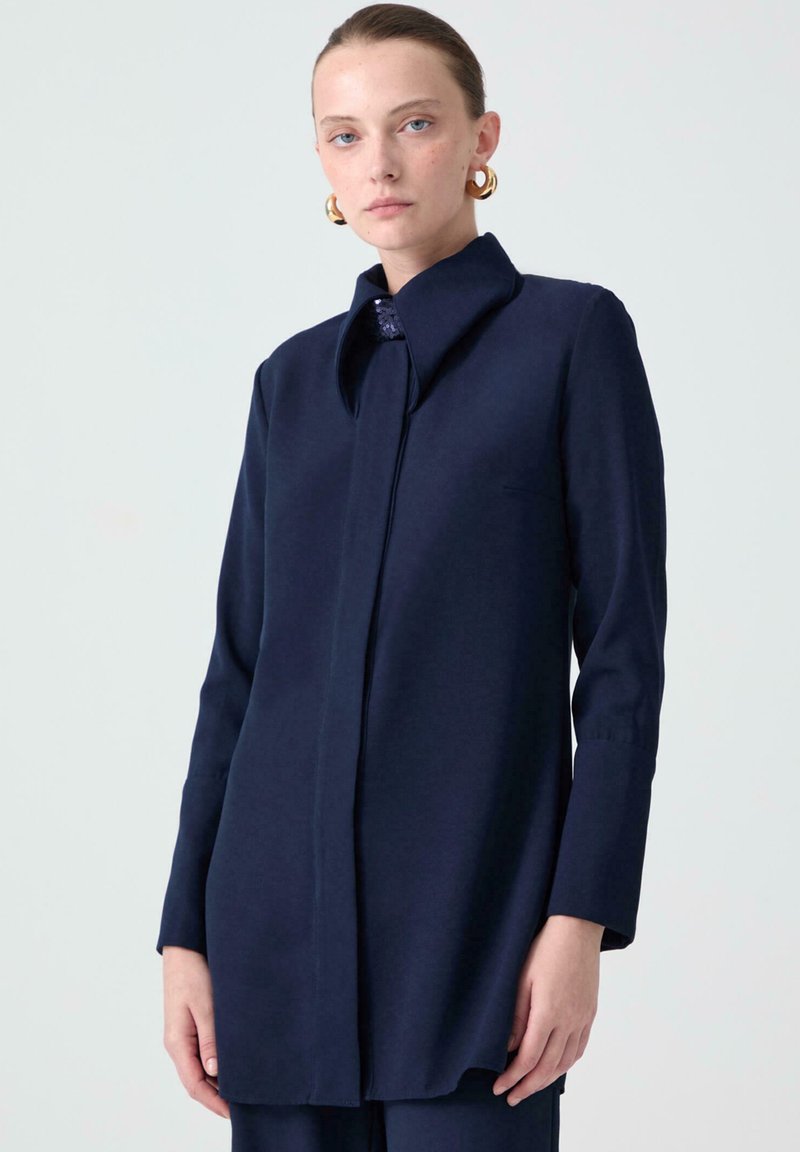 Navy blue long-sleeve shirt with a collar, featuring a straight cut and subtle texture, button closure, and a sleek design.