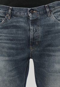 Džínové kalhoty ve středně modré barvě s vybledlou texturou, s klasickými kapsami, zapínáním na knoflík a viditelnými švy.