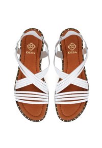 Weiße Riemchensandalen mit brauner Innensohle, versehen mit goldenen Nieten entlang der Kanten und einem Markenlogo auf dem Fußbett.