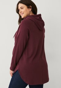 Bordeauxfarbener Hoodie mit Kordelzug, langen Ärmeln und abgerundetem Saum. Aus weichem Stoff gefertigt, mit lockerer Passform und dezenten Nähten.