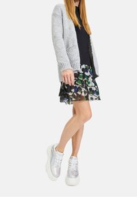 Light gray knitted cardigan over a black ribbed top, paired with a layered, colorful patterned skirt and glossy white platform sneakers.