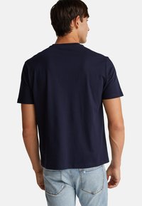 Námořnická modrá bavlněná trička s kulatým výstřihem, krátkými rukávy a rovním lemem. Hladká textura s minimalistickým designem.