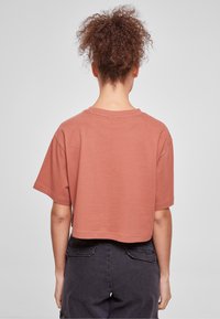 Krátký rukáv, zkrácený tričkový top v barvě rezavé, vyrobený z měkké látky s kulatým výstřihem a švy na lemu.