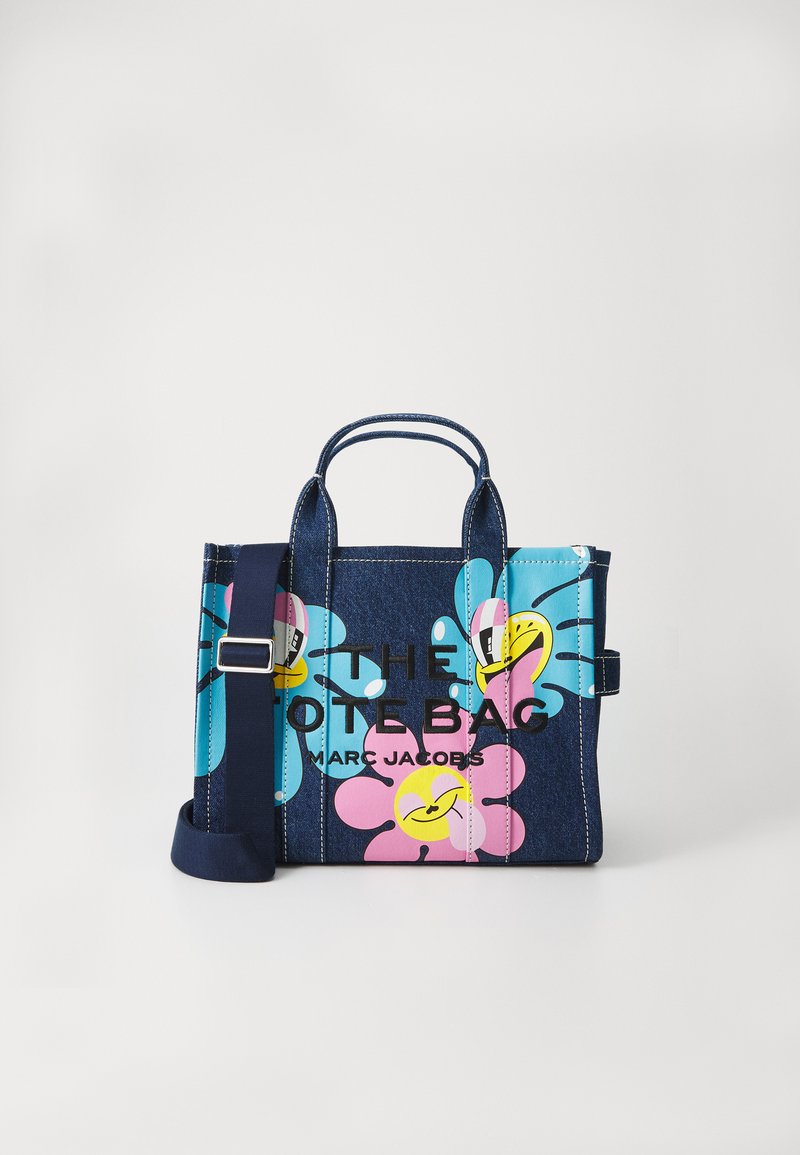 Saco tote de denim com padrões de flores em azul, rosa e amarelo. Possui duas alças e uma alça de ombro ajustável. Logótipo em texto preto.
