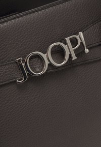 Borsa a tracolla in pelle nera con un evidente accento del logo argento "JOOP!". La superficie è leggermente grinzosa e presenta un design elegante.