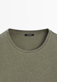 T-shirt vert olive à col rond avec une étiquette noire Massimo Dutti cousue à l'intérieur du col.