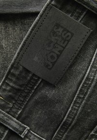 Černá denimová látka se viditelným vzorem švů. Na látce je připevněná texturovaná černá visačka s embosovaným nápisem "Jack & Jones".