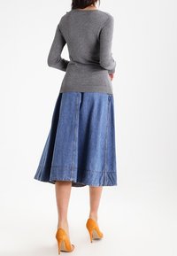 Haut gris à manches longues associé à une jupe midi en denim bleu à la coupe évasée et des chaussures à talons hauts orange. Texture lisse, style décontracté.