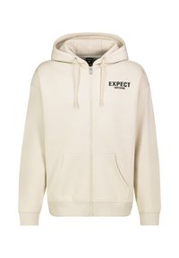 Zippered hoodie in light beige fabric with a soft texture. Features a front pocket, drawstring hood, and black "EXPECT NOTHING" text.