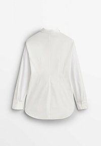 Chemise blanche à manches longues, poignets boutonnés, col classique et ourlet légèrement arrondi. Tissu lisse avec un design épuré et minimaliste.