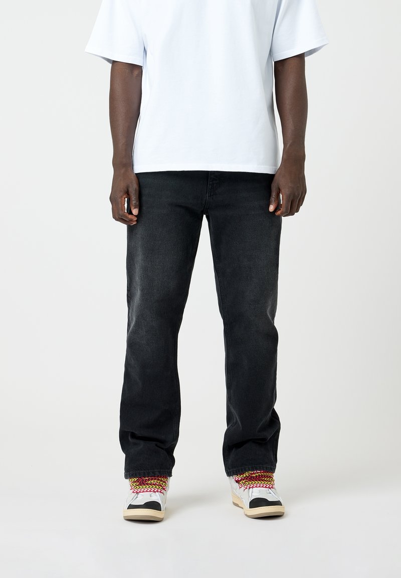 Jeans in denim nero con una vestibilità rilassata, abbinati a una t-shirt oversize azzurro chiaro e sneakers patchwork multicolori.