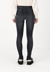 Jeans skinny gris oscuro de cintura alta, con un diseño clásico de cinco bolsillos y una textura suave. Combinados con zapatos de plataforma negros.