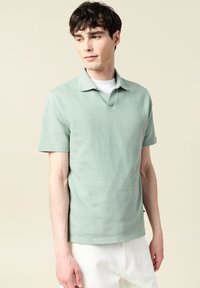 Lyhythihainen poolopaita vaaleahiuksisesta teksturoidusta kankaasta, jossa on kauluksessa V-muotoinen aukko. Yhdistetty vaaleanharmaisiin housuihin.