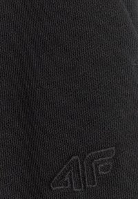 Gros plan sur un tissu noir avec un logo brodé subtil comprenant des lettres stylisées et un design d'aile dans le coin inférieur droit.