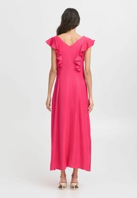 Fuchsiamaxiklänning med V-back, volangärmar och en flödande silhuett. Tillverkad av lättviktig tyg. Enkelt och stilrent design.