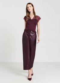 Top bordeaux con pizzo abbinato a pantaloni in pelle a gamba larga dello stesso colore. Tacchi a punta completano l'outfit.