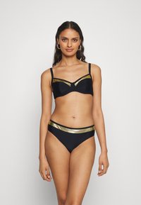 Juodas bikini maudymosi kostiumas su auksiniais akcentais; liemenėlė su laidais turi struktūrizuotą dizainą, o apatinė dalis turi atitinkamą auksinę juostą. Lygi tekstūra.