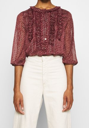 Bordeaux, transparante blouse met gerimpelde kraag en voorkant, verticale strepen en knopen. Gecombineerd met lichtgekleurde, hoge taillebroeken.