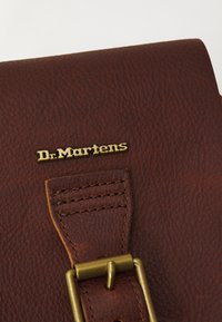Brun texturerad läder med en guldfärgad "Dr. Martens"-logotyp och en metallspänne-design.