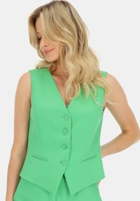 Zielona kamizelka bez rękawów z głębokim dekoltem, z pięcioma guzikami i bocznymi kieszeniami; gładka tekstura i dopasowany krój z kanciastym dołem.