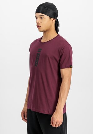 T-shirt en coton bordeaux avec un logo "ALPHA" noir sur le devant et un détail de tag sur le côté. Texture douce et design classique à col rond.