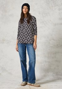 Schwarz-weißer gemusterter Langarmoberteil mit einem Diamantdesign, kombiniert mit hellblauen Schlagjeans und beigen Turnschuhen.