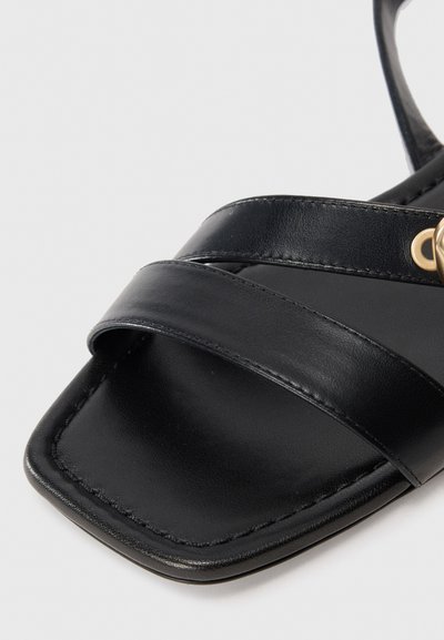 Black leather sandals feature multiple horizontal straps and a square toe design. Gold hardware detail enhances the minimalist style.